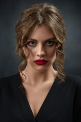 Portrait of young beatiful girl wearing black fashionable shirt and bright red lipstick. Woman having stylish hairdress with curles and green eyes, plump lips. Photo made on dark studio background.