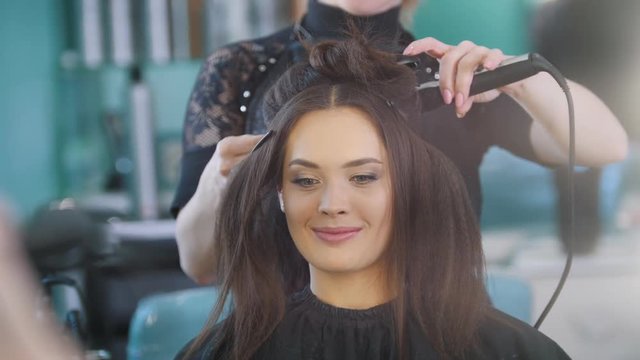 Professional hairstylist creating evening hairstyle for beautiful smiling model