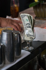 Cash tips in a cocktail glass on bar counter top. Customers give money as thanks for proper service to bartender when ordering and making drinks for patrons at restaurant