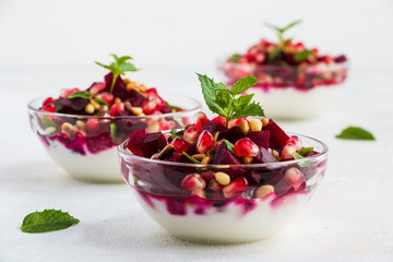 Vitamin vegetarian salad with beets, fried pine nuts, fresh mint and Greek yogurt in small glass bowls on a white table.