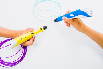 Kids hands holding 3d pens with filaments on white background. Top view