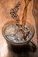 Hot coffee is poured from a Turkish coffee pot into a cup, hands are visible