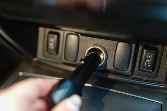 A man connects the device to the cigarette lighter of the car. The man's hand is plugging the car camera or phone adapter into the cigarette lighter into the car.