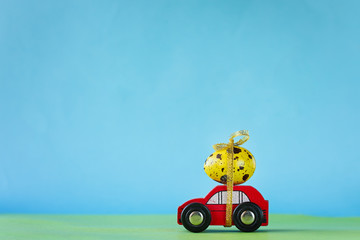 Easter holiday concept - Red toy car carrying yellow egg. Toned picture