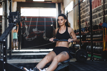 Fototapeta na wymiar Muscular female using rowing machine in fitness club, front view