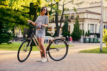 An attractive brunette female with a bicycle in the city park.