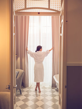 Back view of woman in bathrobe holding curtains in the bathroom