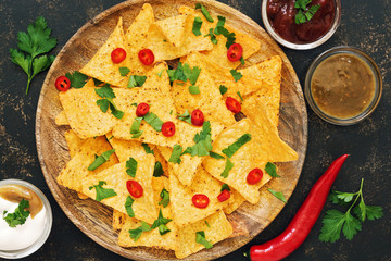 Nachos. Close-up of corn chips with variety of sauces ,chili pepper and greens on dark background. The view from the top, place for text.