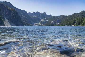 Low angle close up view of alpine lake water in mid day sun with mountains.