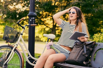 Obraz premium Portrait of an attractive brunette sits on a bench with bicycle 