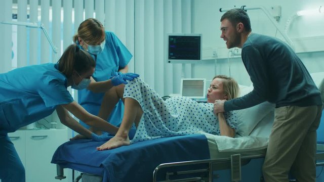 In the Hospital, Woman in Labor Gives Birth, Obstetricians and Doctors Assist, Her Husband Supports Her by Holding Hand. Modern Technologically Advanced Maternity Ward with Professional Midwives. 
