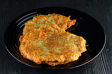 potato pancakes, on a black plate on a wooden background. Home kitchen.