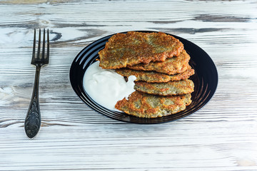 potato pancakes with sour cream, on a black plate on a wooden background. Home kitchen.