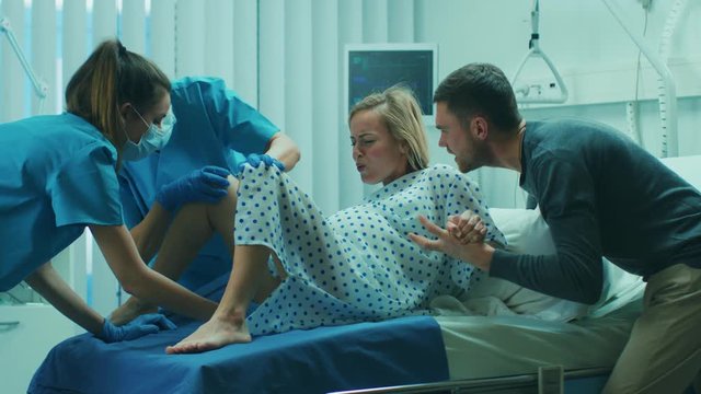 In the Hospital, Woman in Labor Pushes to Give Birth, Obstetricians and Doctors Assist, Her Husband Supports Her by Holding Hand. Shot on RED EPIC-W 8K Helium Cinema Camera.