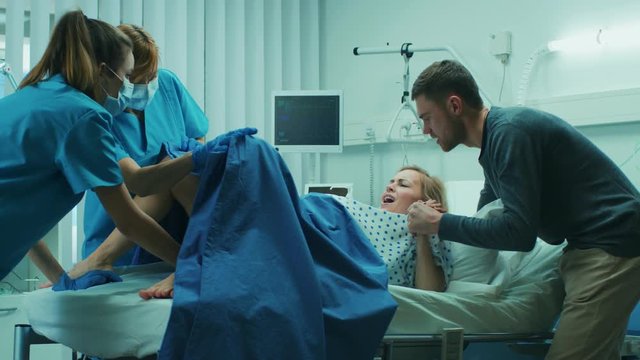 In the Hospital, Woman in Labor Pushes to Give Birth, Obstetricians Assisting, Spouse Holds Her Hand. Modern Maternity Hospital with Professional Midwives. Shot on RED EPIC-W 8K Helium Cinema Camera.