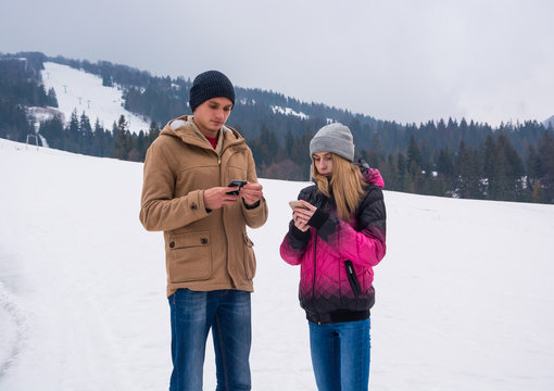 A young guy and a girl who look at their smartphones against the backdrop of a mountain landscape