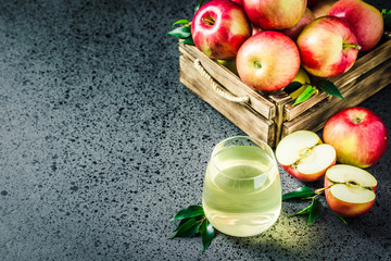 Apple cider and fresh apples in wooden box on concrete background. Selective focus, space for text.