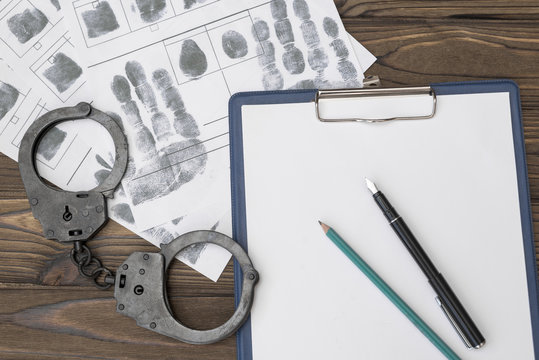 handcuffs, fingerprint map, blank sheet of paper on a wooden background. a crime. arrest.