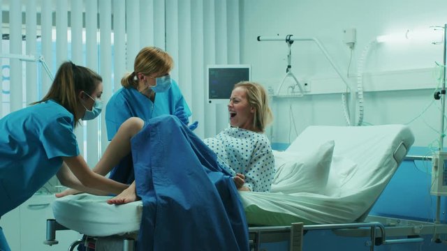 In the Hospital Woman in Labor Pushes to Give Birth, Obstetricians Assisting and Instructing Her. Modern Maternity Hospital with Professional Midwives. Shot on RED EPIC-W 8K Helium Cinema Camera.