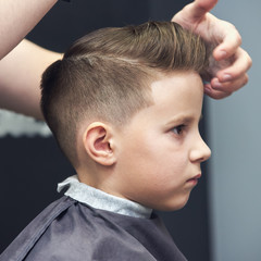 Barber shop. Hairdresser makes hairstyle to a boy using styling gel. - 197393728