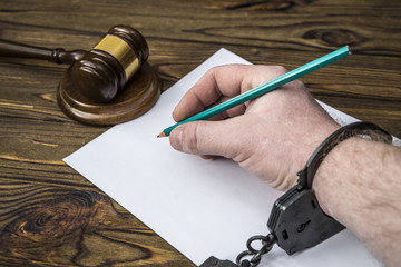 hands of the criminal in handcuffs. writing on a sheet of paper a confession of a crime, an...