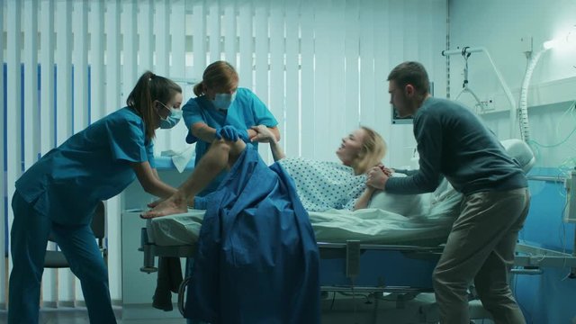 In the Hospital Woman in Labor Pushes to Give Birth, Obstetricians Assisting, Husband Supports Her by Holding Hand. Shot on RED EPIC-W 8K Helium Cinema Camera.