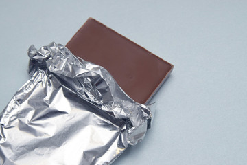 Chocolate Bar Tablet Wrapped in Aluminum Foil over Gray Neutral Background with copy space. Sweet...