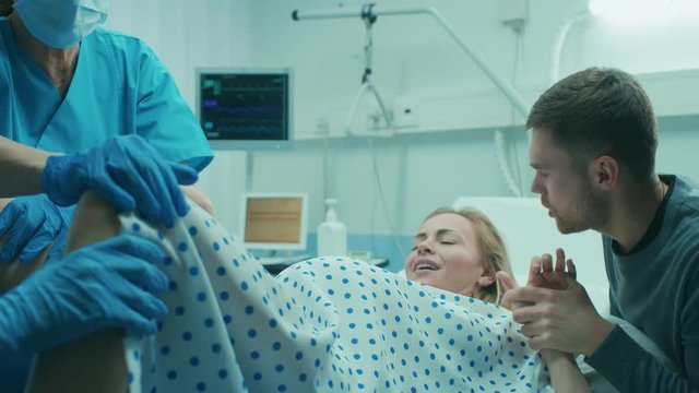 In the Hospital Woman in Labor Pushes to Give Birth, Obstetricians Assisting, Husband Holds Her Hand for Support. Shot on RED EPIC-W 8K Helium Cinema Camera.