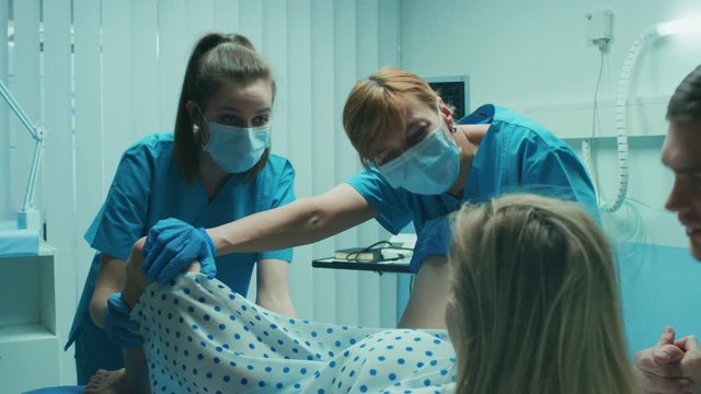 In the Hospital Woman in Labor Pushes to Give Birth, Obstetricians Assisting, Husband Holds Her Hand. Modern Delivery Ward with Professional Midwives. Shot on RED EPIC-W 8K Helium Cinema Camera.