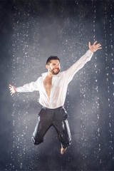 Naklejka na ściany i meble Attractive bearded young man jumping for joy under the rain