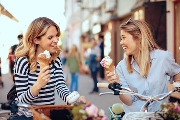 Two young women holding ice cream in the city on a sunny day