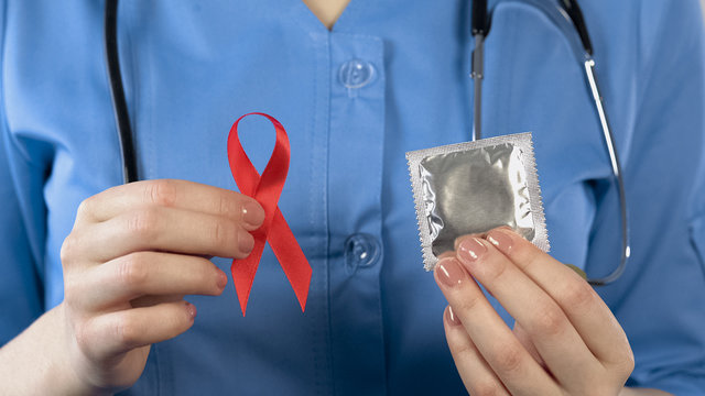 Doctor warning about AIDS disease showing red ribbon and condom, health campaign