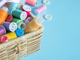Colorful sewing buttons and thread in a wooden box on a blue background.