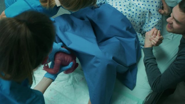 In the Hospital Woman in Labor Pushes to Give Birth, Obstetricians Pulling Baby Out During Delivery, Husband Holds Her Hand for Support. Shot on RED EPIC-W 8K Helium Cinema Camera.