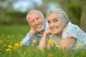 senior couple lying on green meadow with dandelions