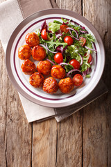 fried glazed meatballs served with salad of lettuce, cherry tomatoes and onions close-up on a plate. Vertical top view
