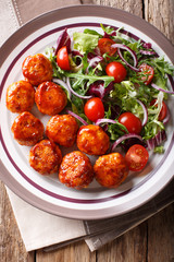 Tasty glazed meatballs with fresh vegetable salad close-up on a plate. Vertical top view