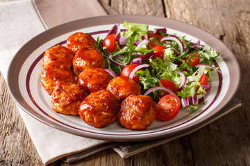 fried glazed meatballs served with salad of lettuce, cherry tomatoes and onions close-up on a plate. horizontal