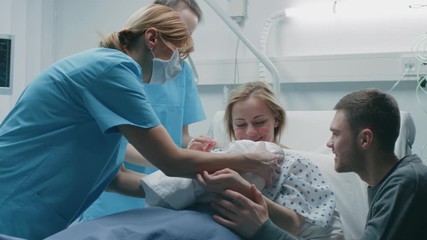 In the Hospital Midwife Gives Newborn Baby to a Mother to Hold, Supportive Father Lovingly Hugging Baby and Wife. Happy Family in the Modern Delivery Ward. Shot on RED EPIC-W 8K Helium Cinema Camera. - Powered by Adobe