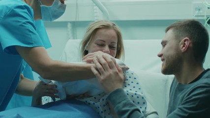 In the Hospital Midwife Gives Newborn Baby to a Mother to Hold, Supportive Father Lovingly Hugging Baby and Wife. Happy Family in the Modern Delivery Ward. Shot on RED EPIC-W 8K Helium Cinema Camera. - Powered by Adobe