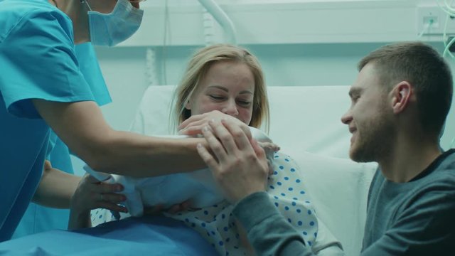 In the Hospital Midwife Gives Newborn Baby to a Mother to Hold, Supportive Father Lovingly Hugging Baby and Wife. Happy Family in the Modern Delivery Ward. Shot on RED EPIC-W 8K Helium Cinema Camera.