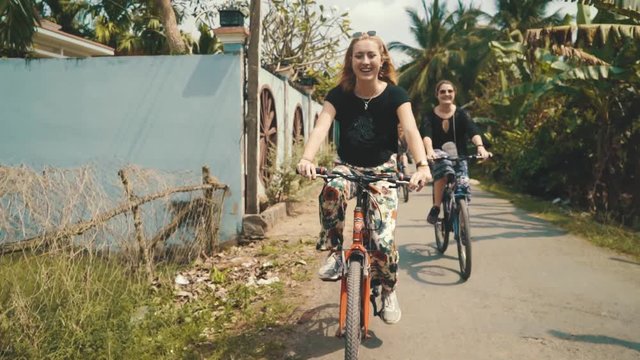 Slow motion shot of two young blonde women riding bicycles with their friends through Vietnam while on vacation on a sunny day