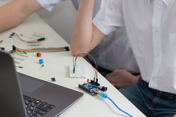 A boy teenager with a teacher collect robot arduino and program it on the computer. The boards and microcontrollers are on the table. STEM education. Programming. Mathematics. The science. Technologie