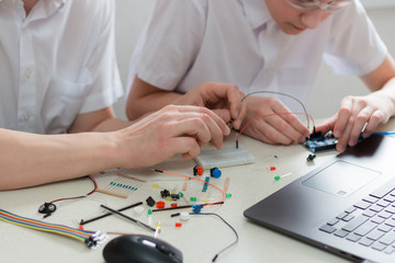 A boy teenager with a teacher collect robot arduino and program it on the computer. The boards and microcontrollers are on the table. STEM education. Programming. Mathematics. The science. Technologie