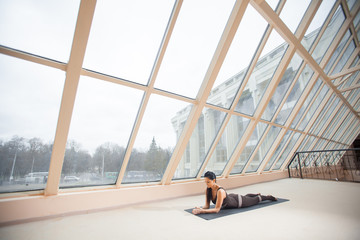 Brunette woman practicing yoga concept, stretching in Cobra exercise, Bhujangasana pose in front of large windows. working out, fu