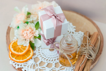 Made at home from orange oil with cinnamon perfume in a glass jar. Slices of dried orange, dried cinnamon and flowers. Gift box with jewelry charm bracelet is on the table. Present for every woman.
