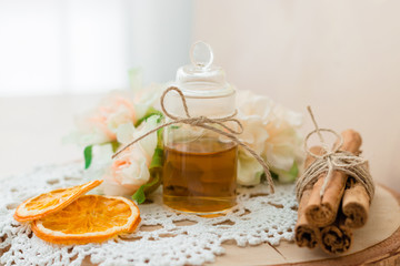 Made at home from orange oil with cinnamon perfume in a glass jar. Slices of dried orange, dried cinnamon and flowers. Crocheted white napkin. Perfumer.Natural and healthy cosmetic. Wooden background.