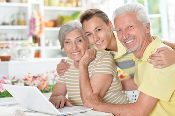 happy senior couple with grandson using laptop
