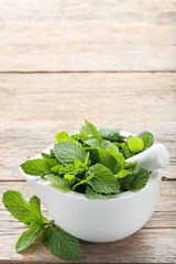 Fresh mint leafs in mortar on grey wooden table