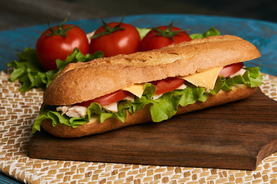 Fresh submarine sandwich with chicken fillet, cheese, fresh tomatoes, lettuce, cucumbers and onions on wooden background